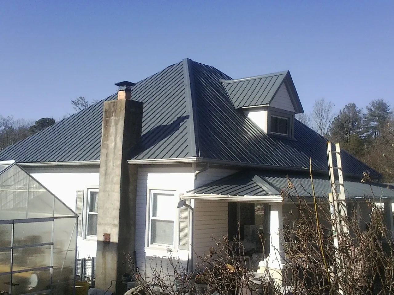 Dark blue standing seam metal roof on a white farmhouse with dormer — Slate & Tile Roof Repair by Roofing Brothers in Rogerson