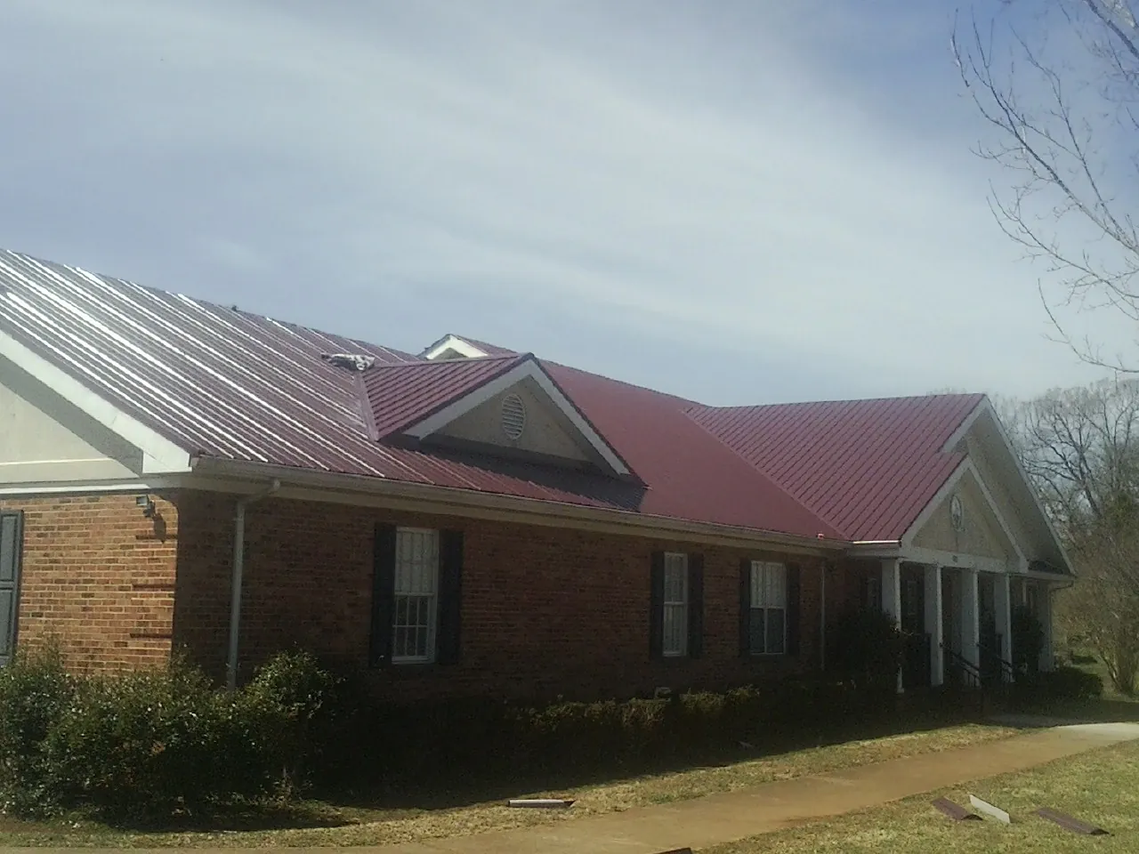 Red metal roof with gabled entries on a long brick building, from a Hail Damage Roof Repair job in Rogerson