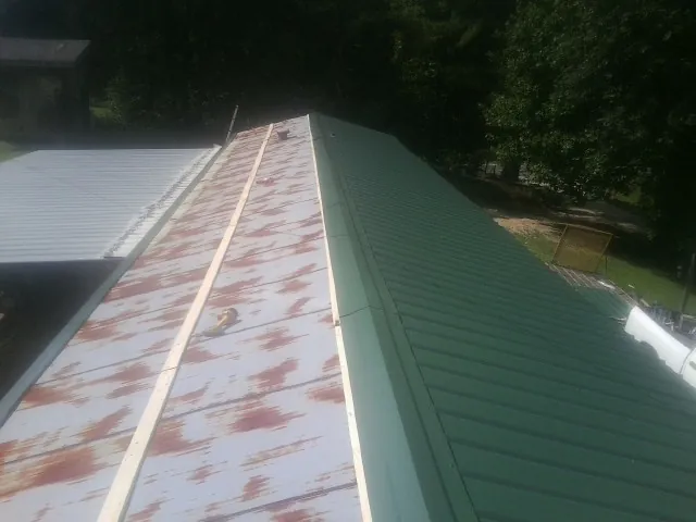 Old rusted panels beside newly installed green metal roofing — Wind Damage Roof Repair by Roofing Brothers in Rogerson
