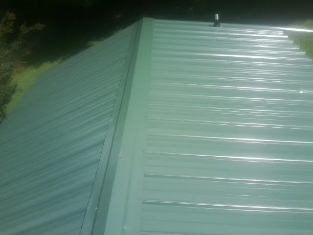 New green metal panels meeting at the ridge of a roof — Flat Roof Repair work by our crew in Rogerson