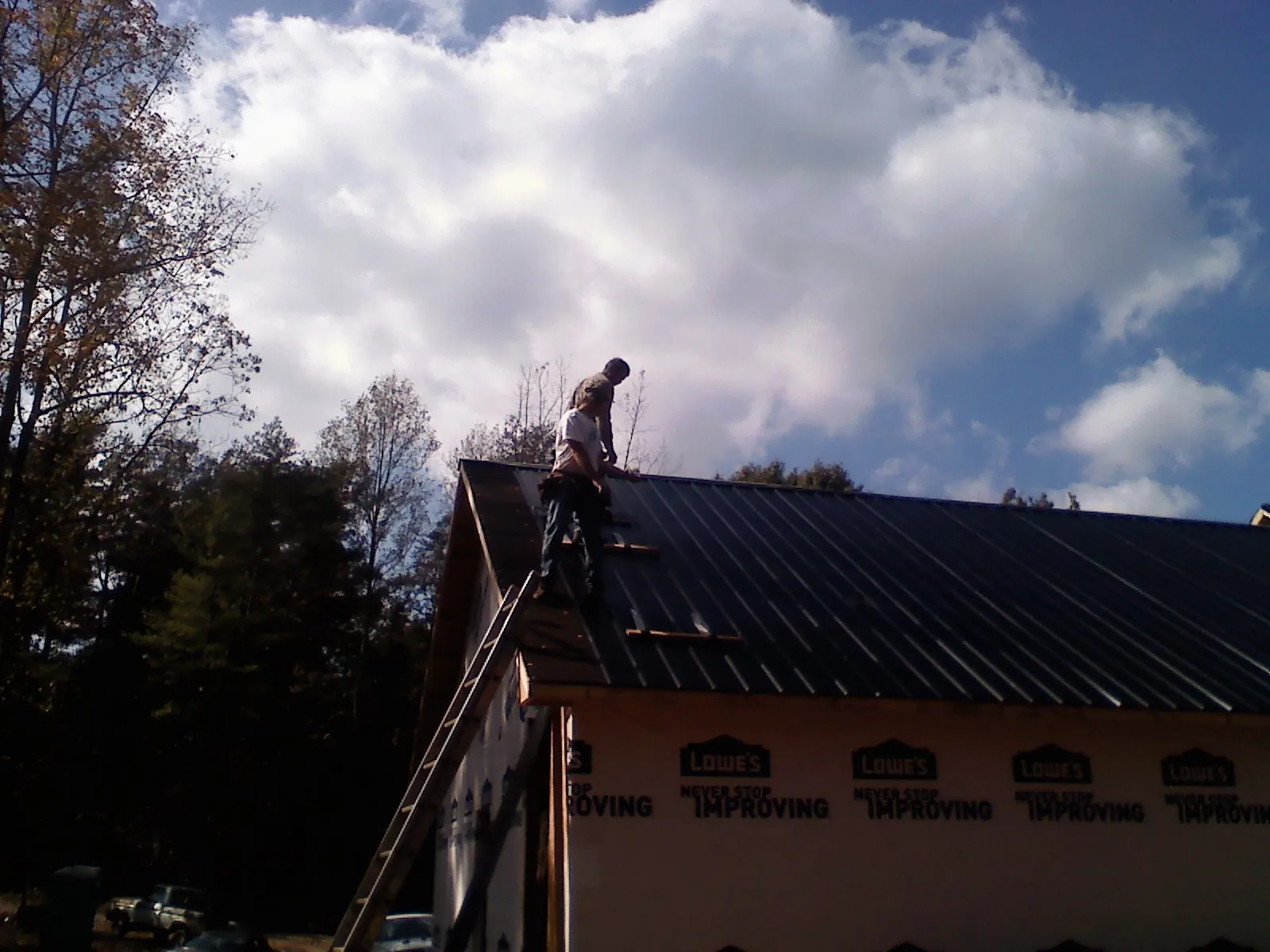 Roofer fastening dark metal panels high against a cloudy sky, from a Roof Inspection job in Rogerson